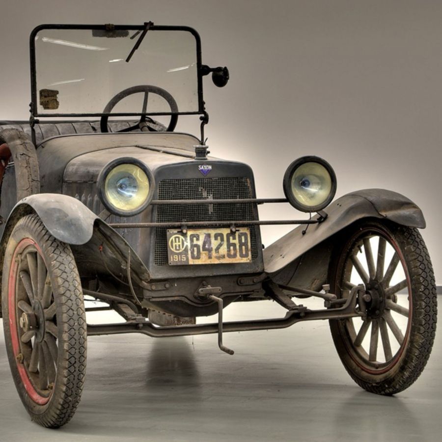 Ein vintage Auto aus dem Jahr 1915, bekannt als Saxon. Es hat eine quadratische Motorhaube, runde Scheinwerfer und eine schwarze Karosserie mit sichtbarem Verschleiß. Das Nummernschild zeigt die Zahlen 64268, und das Fahrzeug steht auf einem neutralen Hintergrund.
